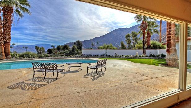 Blick von einer Terrasse mit Pool auf eine Berglandschaft mit Palmen.