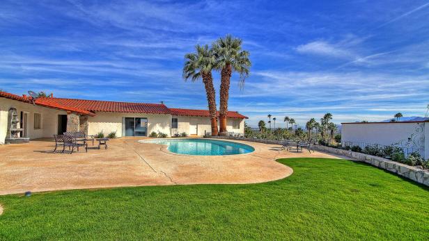Ein Haus mit Pool und Palmen unter blauem Himmel.
