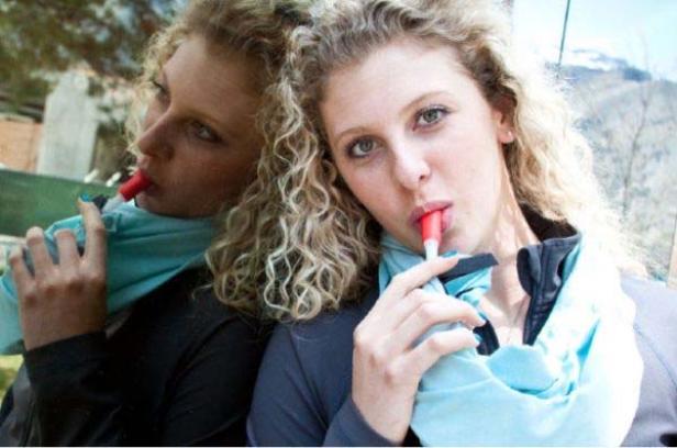 Eine Frau mit blonden Locken trinkt mit einem Strohhalm aus einer Trinkflasche, die sie um den Hals trägt.