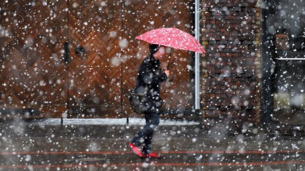 Eine Person mit rotem Schirm und roten Schuhen geht durch starken Schneefall.