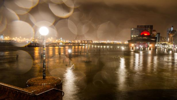 Die Hamburger Landungsbrücken bei Nacht und Regen beleuchtet.