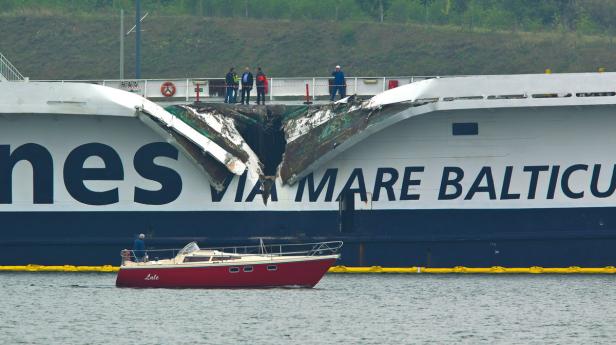 Eine kleine rote Segelyacht fährt vor einem beschädigten Fährschiff der Reederei Polferries.