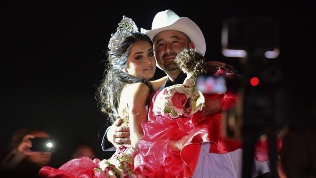 Ein Vater mit Cowboyhut umarmt seine Tochter mit Krone und Puppe.