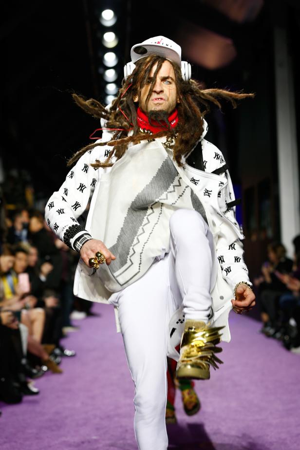 Ein Mann mit Dreadlocks läuft auf einem Laufsteg und trägt auffällige goldene Schuhe.
