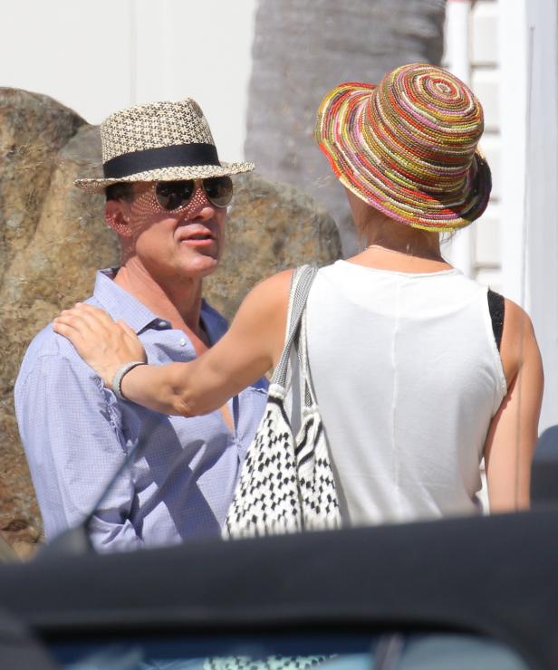 Ein Mann mit Hut und Sonnenbrille wird von einer Frau mit einem bunten Hut berührt.