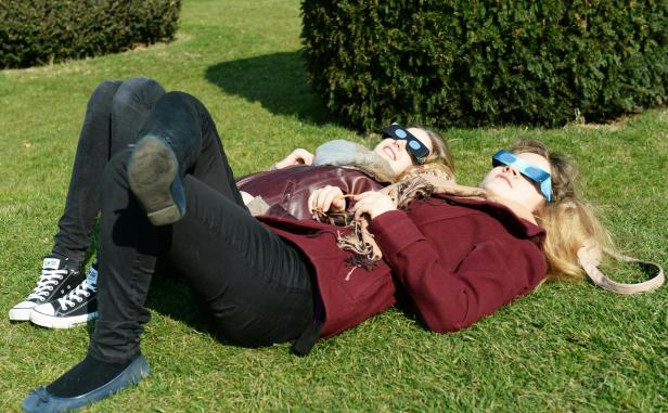 Zwei Frauen liegen mit Sonnenfinsternisbrillen auf einer Wiese.