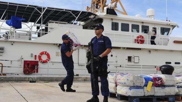 Zwei Küstenwachebeamte stehen neben beschlagnahmten Säcken vor einem Schiff.