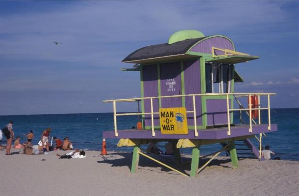 Ein farbenfroher Rettungsschwimmerstand am Strand von Miami mit Badegästen im Hintergrund.