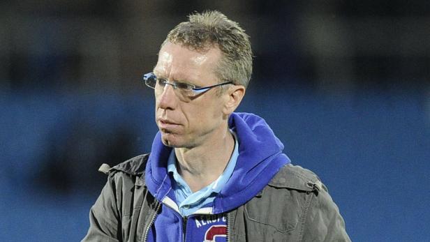 Ein Mann mit Brille und Jacke vor einem blauen Hintergrund.