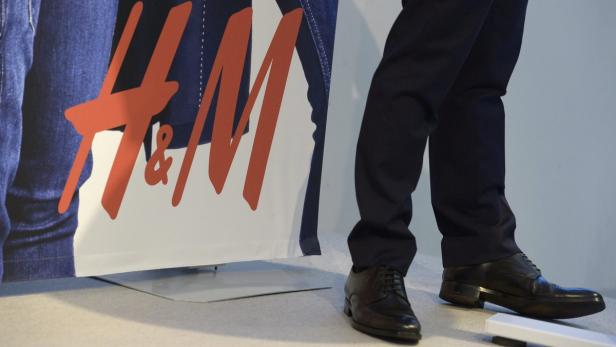 Ein Mann in Anzughose und Lederschuhen steht vor einem H&M-Werbeplakat.