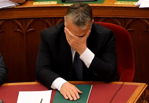 Ein Mann im Anzug sitzt an einem Tisch und verdeckt sein Gesicht mit der Hand.