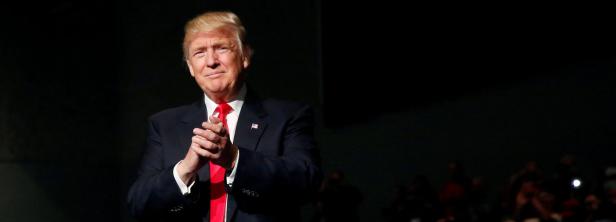 Donald Trump klatscht vor einem dunklen Hintergrund in die Hände.