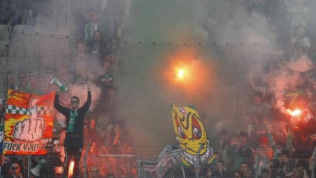 Fußballfans zünden Bengalos und schwenken Fahnen hinter einem Netz.