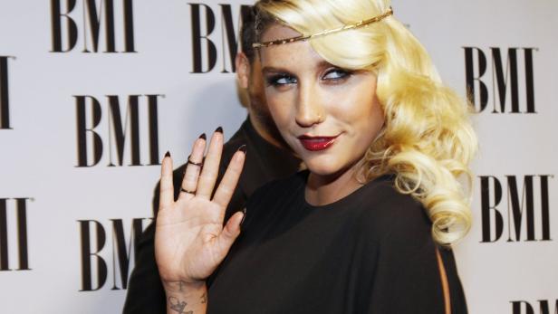 Die Sängerin Kesha mit blonden Locken und einem goldenen Haarband winkt in die Kamera.