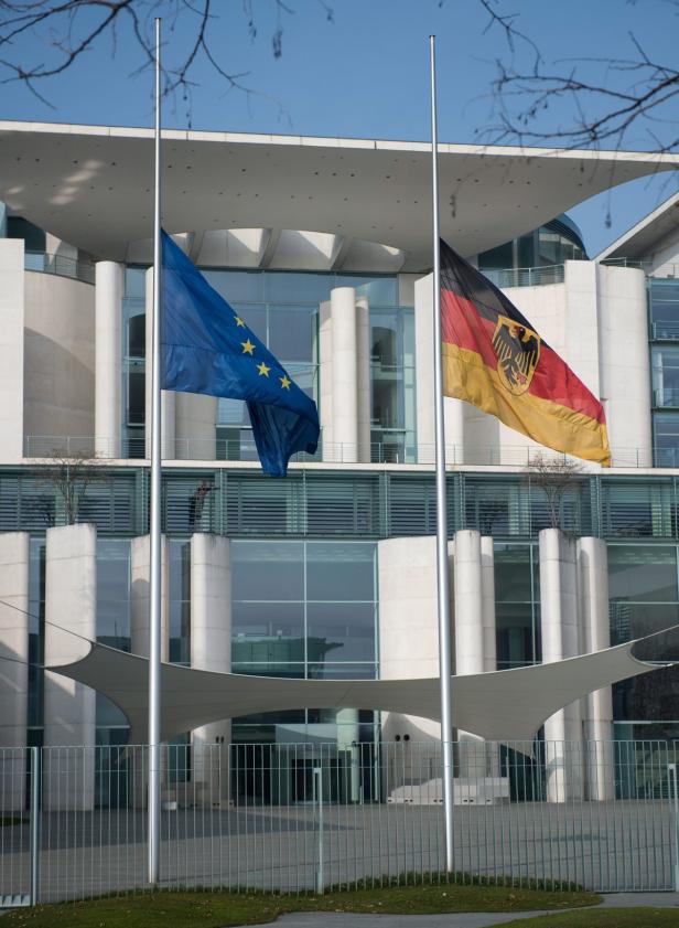 Die Europa- und Deutschlandflagge wehen vor einem modernen Gebäude.