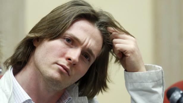 Ein Mann mit langen braunen Haaren blickt nachdenklich in die Kamera.