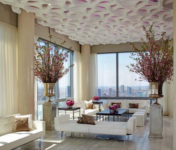 Ein luxuriöser Wohnraum mit weißen Sofas, großen Fenstern und blühenden Kirschzweigen in silbernen Vasen.