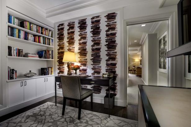 Ein Arbeitszimmer mit einem Schreibtisch vor einer Wand mit Bücherstapel-Tapete.