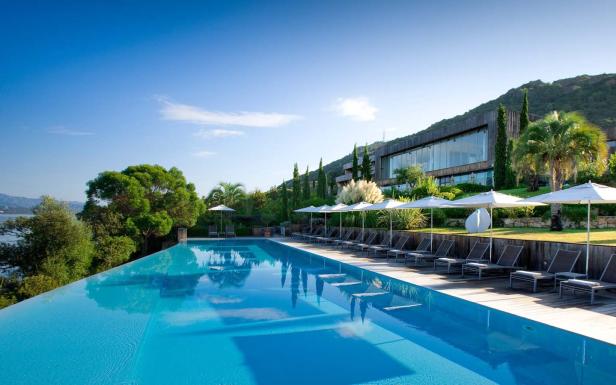 Ein Infinity-Pool mit Liegestühlen und Sonnenschirmen vor einem Hotelgebäude.