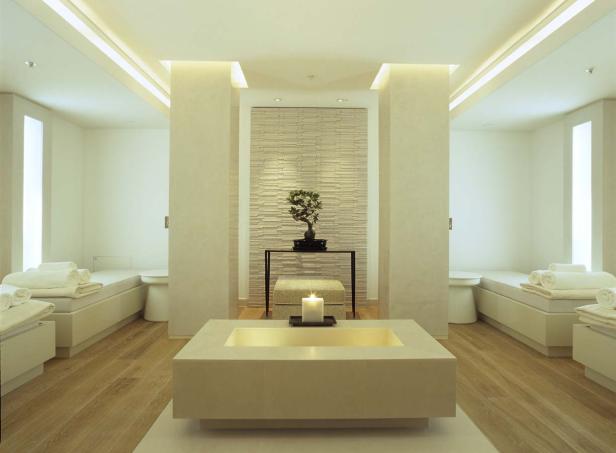 Ein Spa-Raum mit Liegen, Handtüchern, einem Bonsai-Baum und einer Kerze.