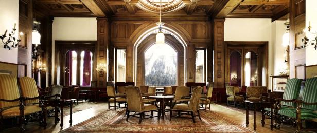 Ein holzgetäfelter Salon mit Tischen und Stühlen auf einem gemusterten Teppich.