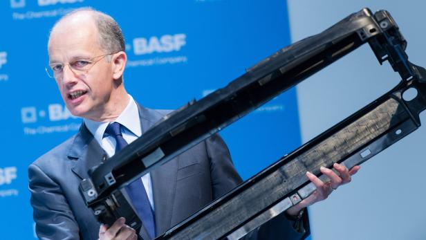 Ein Mann im Anzug präsentiert ein schwarzes Kunststoffteil vor einem BASF-Logo.