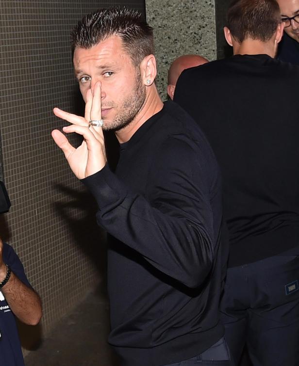 Ein Mann mit dunklem Pullover und großem Ring gestikuliert.