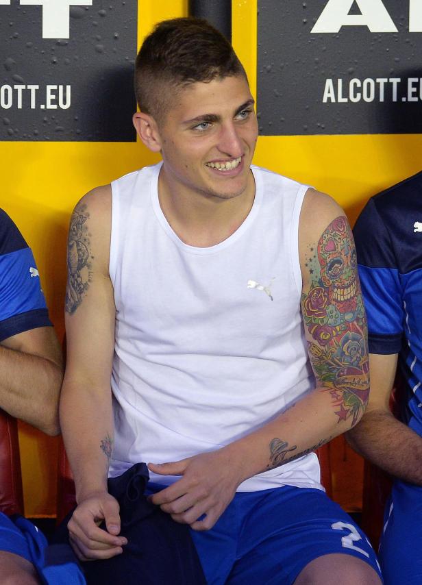 Ein lächelnder Mann mit Tattoos sitzt auf einer Bank.