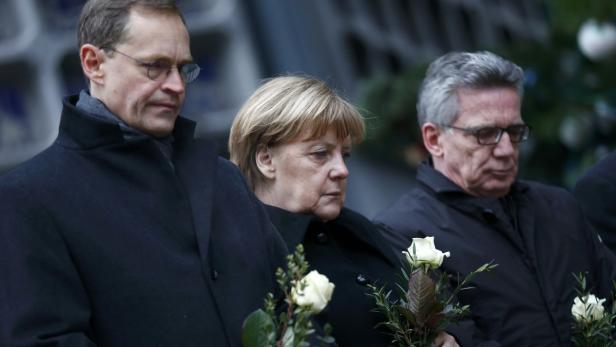 Angela Merkel und andere Personen halten weiße Rosen bei einer Gedenkveranstaltung.