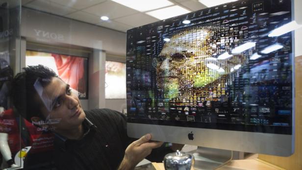 Ein Mann betrachtet einen iMac, dessen Bildschirm ein aus Icons zusammengesetztes Gesicht zeigt.