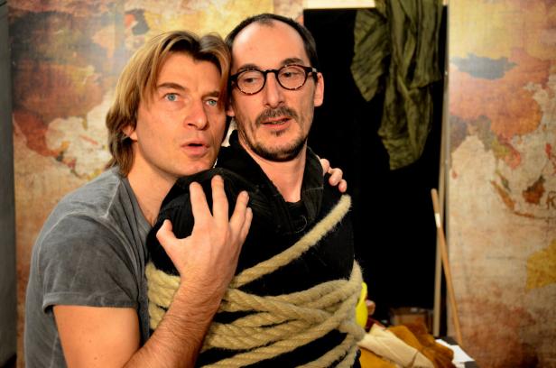 Ein Mann umarmt einen gefesselten Mann vor einer Weltkarte.