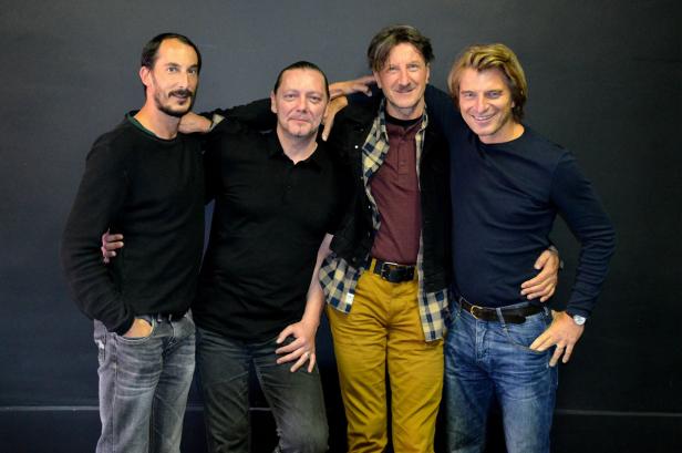 Vier Männer posieren vor einer dunklen Wand für ein Gruppenfoto.