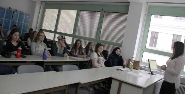 Eine junge Frau hält einen Vortrag vor einer Gruppe von Studenten in einem Klassenzimmer.