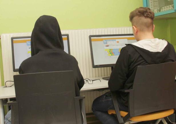 Zwei Jugendliche sitzen vor Computern in einem Raum.