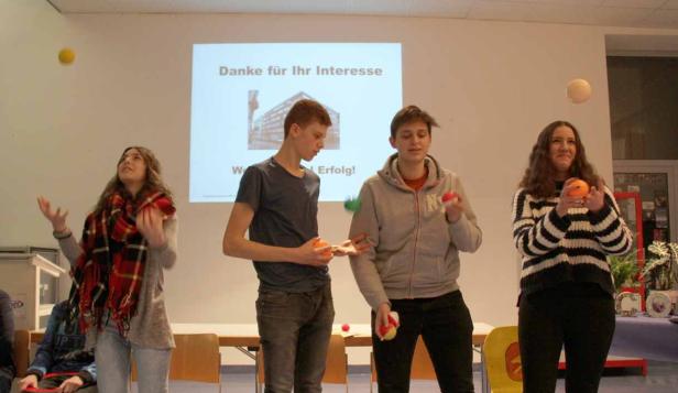 Vier junge Leute jonglieren mit Bällen vor einer Leinwand mit der Aufschrift „Danke für Ihr Interesse“.