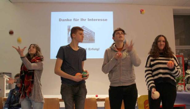 Vier Jugendliche jonglieren mit Bällen vor einer Leinwand mit der Aufschrift „Danke für Ihr Interesse“.