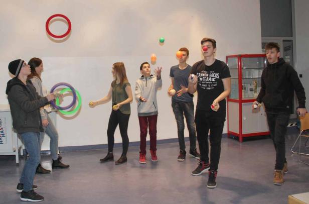 Eine Gruppe Jugendlicher jongliert mit Bällen und Ringen in einem Raum.
