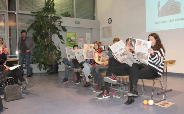 Eine Gruppe von Studenten liest Zeitungen in einem Wartebereich.