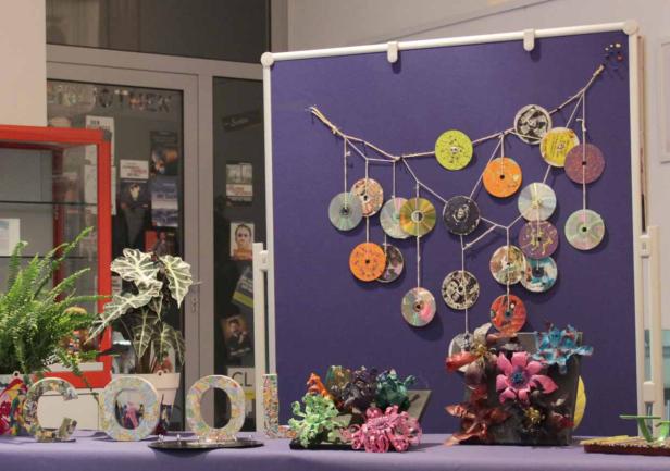 Eine Ausstellung mit recycelten CDs und bunten Dekorationen auf einem lila Tisch.