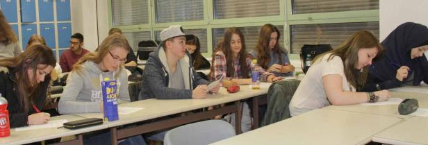 Schüler sitzen in einem Klassenzimmer und schreiben an ihren Tischen.