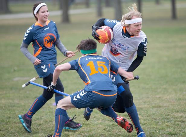 Drei Quidditch-Spieler kämpfen um den Ball auf einem grünen Feld.