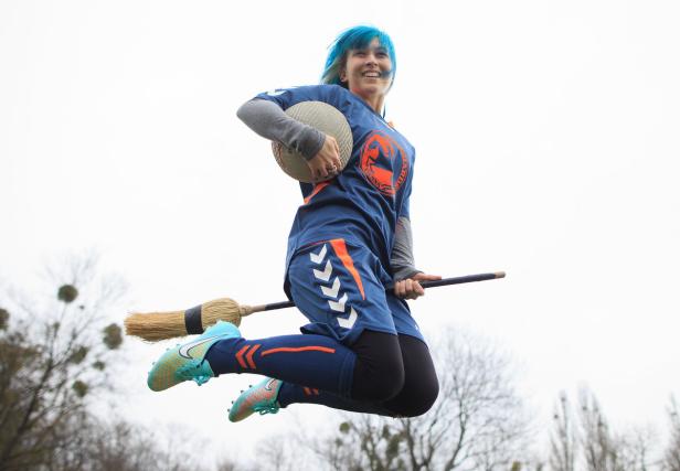 Eine Frau mit blauen Haaren reitet auf einem Besen und hält einen Ball in der Hand.