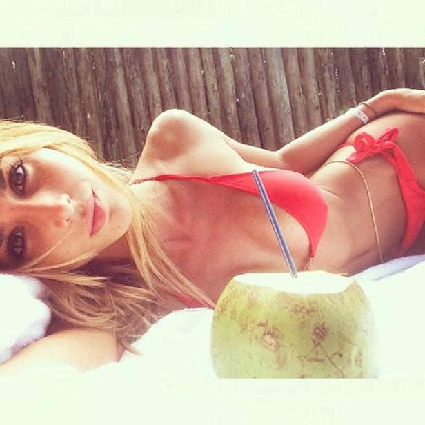 Eine Frau im roten Bikini entspannt mit einer Kokosnuss am Strand.