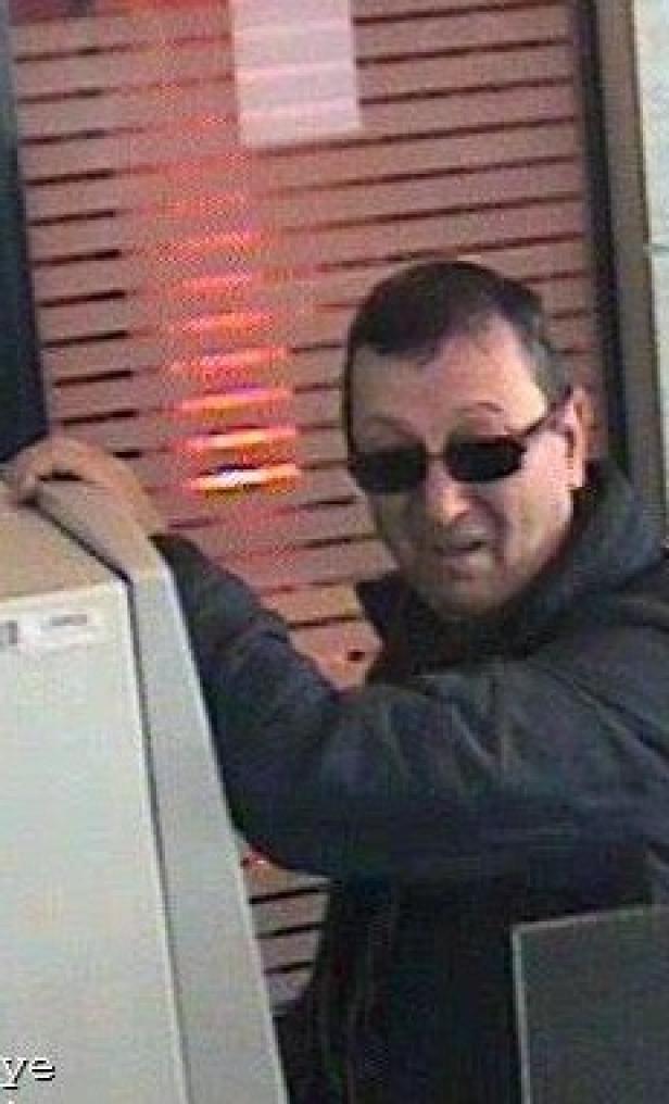 Ein Mann mit Sonnenbrille steht an einem Geldautomaten.