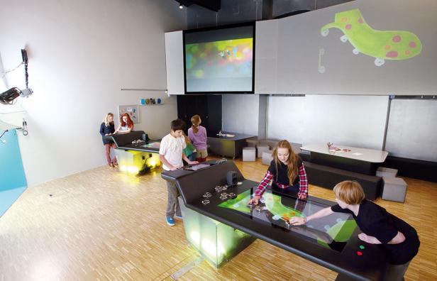 Kinder interagieren mit interaktiven Tischen in einem hellen Raum.