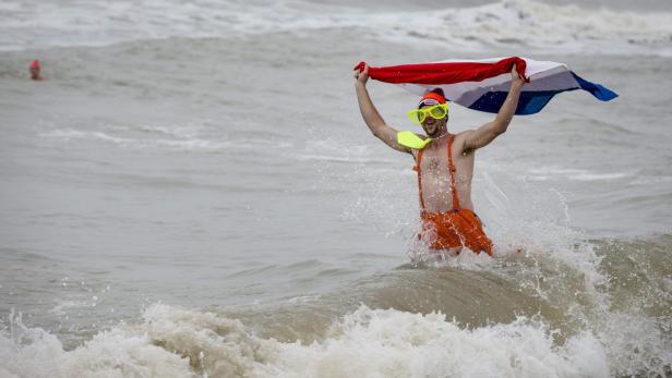 Ein Mann mit Sonnenbrille und niederländischer Flagge steht im Meer.