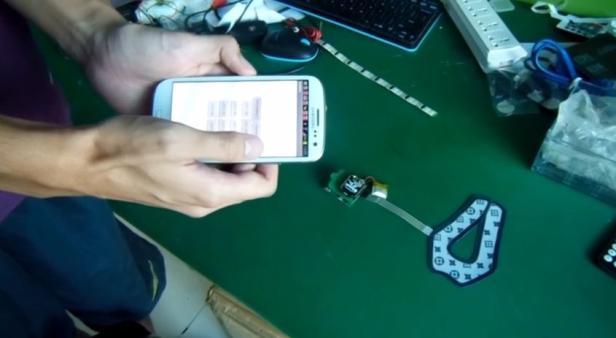 Eine Person fotografiert mit einem Smartphone ein elektronisches Bauteil mit einem Muster.