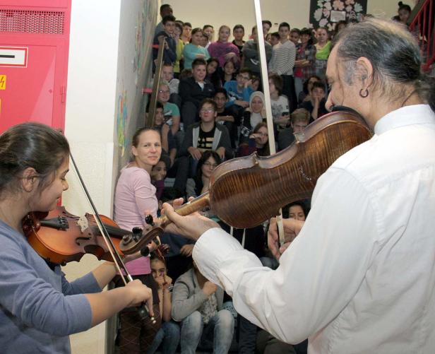 Eine junge Frau und ein Mann spielen Geige vor einer Gruppe von Zuschauern auf einer Treppe.