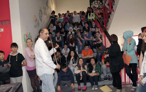 Ein Mann spielt Geige vor einer Gruppe von Schülern auf einer Treppe.