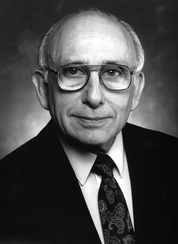 Ein älterer Mann mit Brille und Anzug in Schwarzweiß.